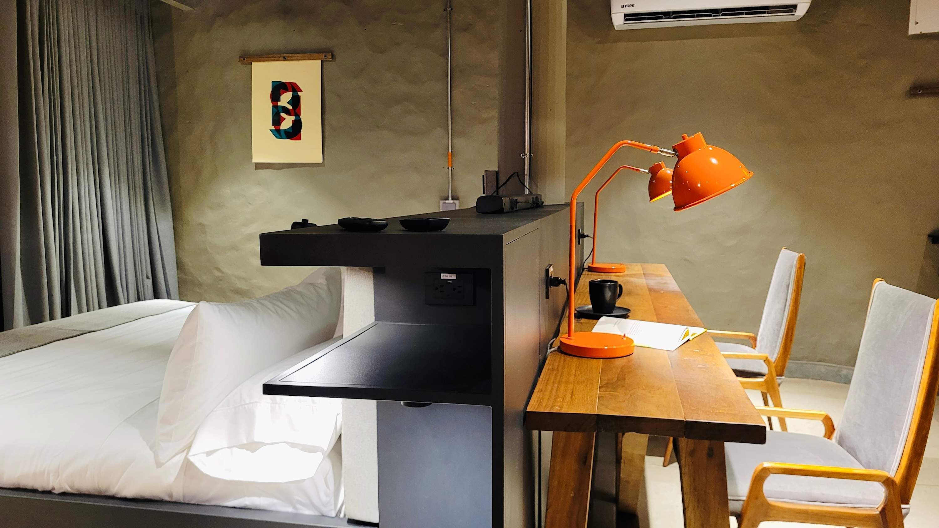 Ein kleines Hotelzimmer mit einem Bett, einem Schreibtisch, einem Stuhl und einer Schreibtischlampe.