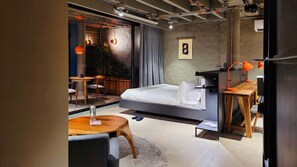 A modern hotel room with a bed, a desk, a chair, and a small table. There is a window with curtains, a plant, and a wall-mounted artwork. - w Elegant Loft w Amazing Deco in Poblado (Medellín)
