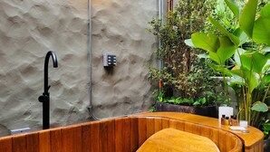 Een houten bad met een zwarte kraan en bedieningspaneel op een structuurwand.