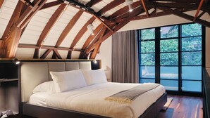Een slaapkamer met een groot bed, houten balken en een raam met uitzicht op groen.