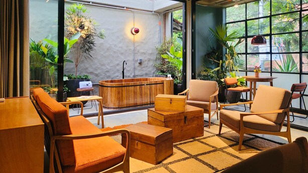 Een knus interieur met een houten badkuip, comfortabele zitplaatsen en grote ramen met uitzicht op groen.