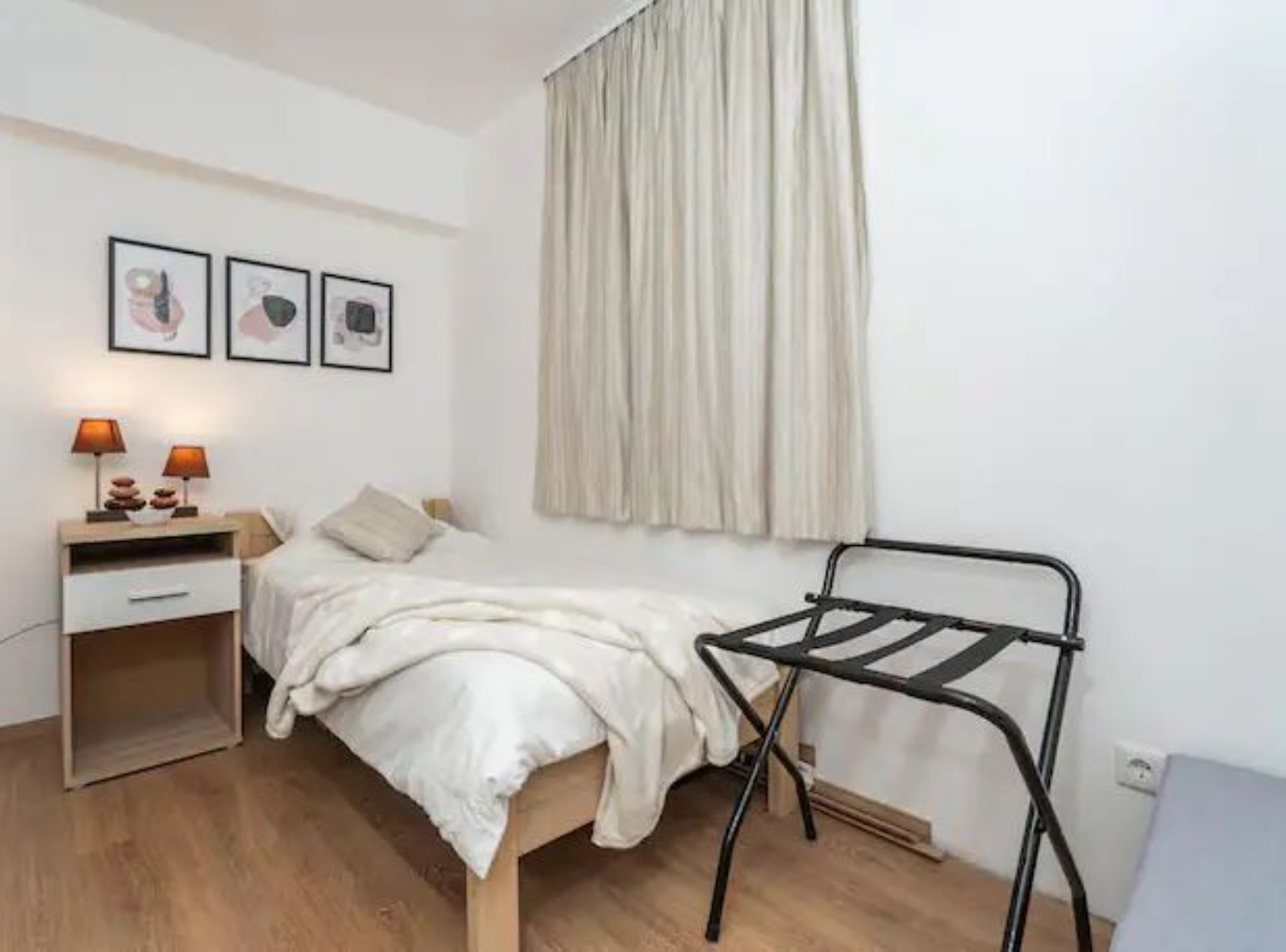 A bedroom with a bed, bedside table, lamp, and a metal drying rack.