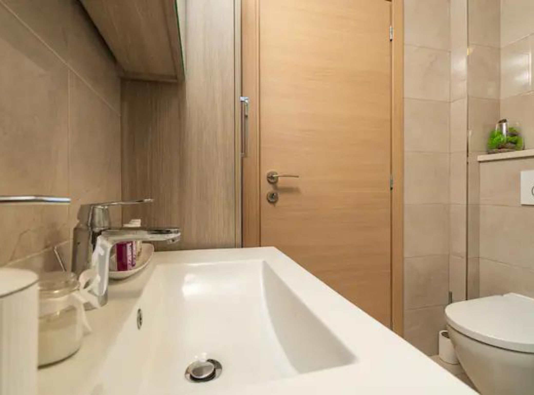 Un baño moderno con un lavamanos grande de color blanco, un inodoro y una puerta de madera.