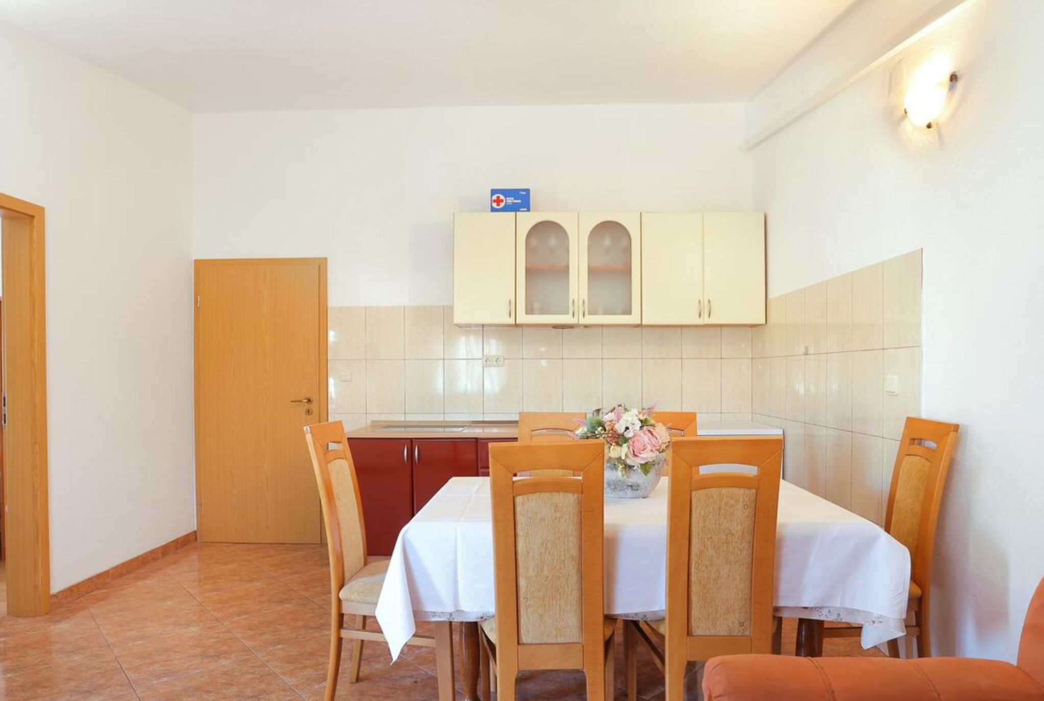 A dining area with a table set for four, surrounded by wooden chairs, and a cabinet above the table.