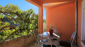 An outdoor patio with a table and chairs, surrounded by orange walls and a view of greenery. - Holiday Home Nada Rogoznica (Rogoznica)