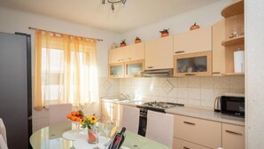 A compact kitchen with a dining area, featuring a glass table, a stove, and cabinets. - Omis River & Sea Escape (Omis)