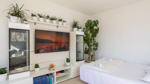 A modern bedroom with a bed, a mounted TV, a bookshelf, and several potted plants. - Omis River & Sea Escape (Omis)