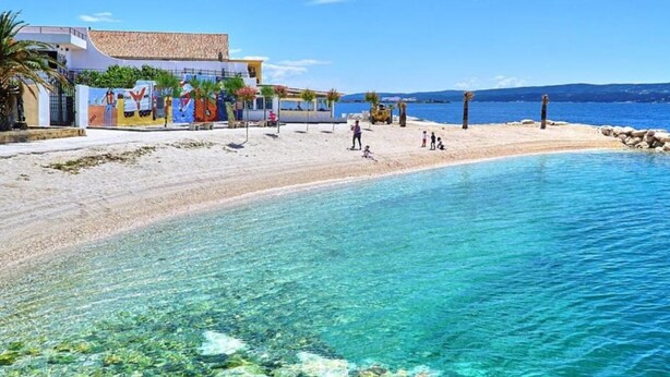 A beach with clear blue water, a sandy shore, and a building with colorful murals. - Omis River & Sea Escape (Omis)