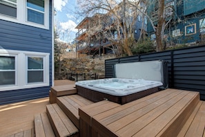 Een hottub met houten banken, een stenen muur en een gebouw met meerdere ramen en balkons op de achtergrond.