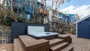 Ein Whirlpool auf einer Holzterrasse mit Stufen, umgeben von Bäumen und einer Steinmauer.
