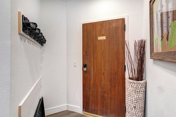 Puerta de madera con un letrero, zapatero y un jarrón decorativo con ramas.