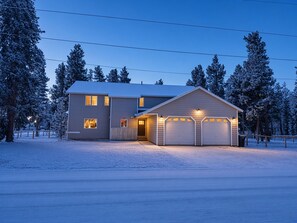 Een twee verdiepingen tellend huis met een garage, omgeven door met sneeuw bedekte bomen.