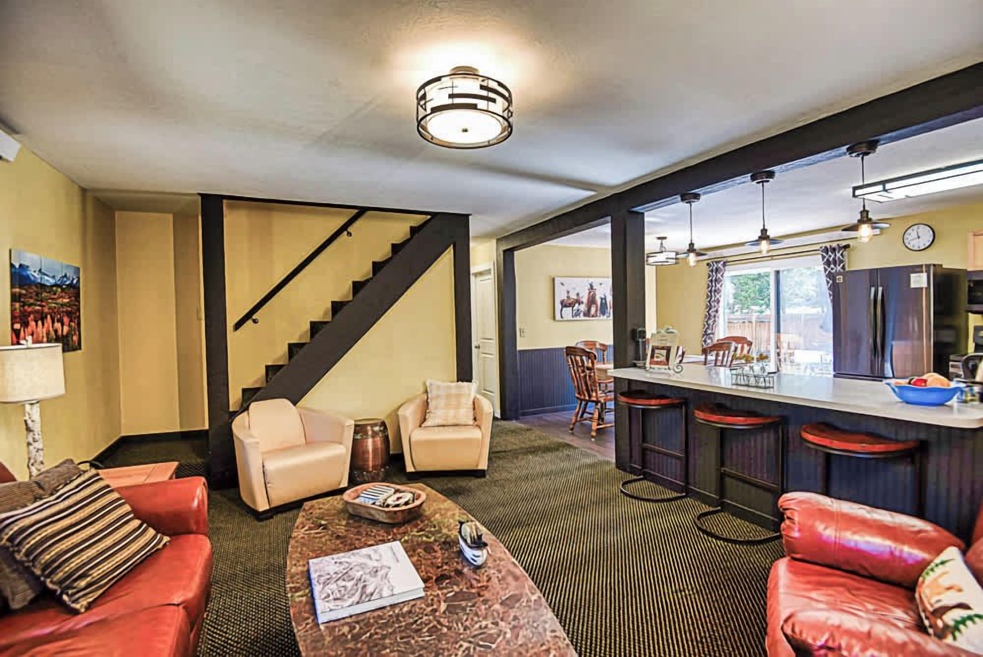 A hotel room with a living area, a kitchen with bar stools, a staircase, and a dining area.