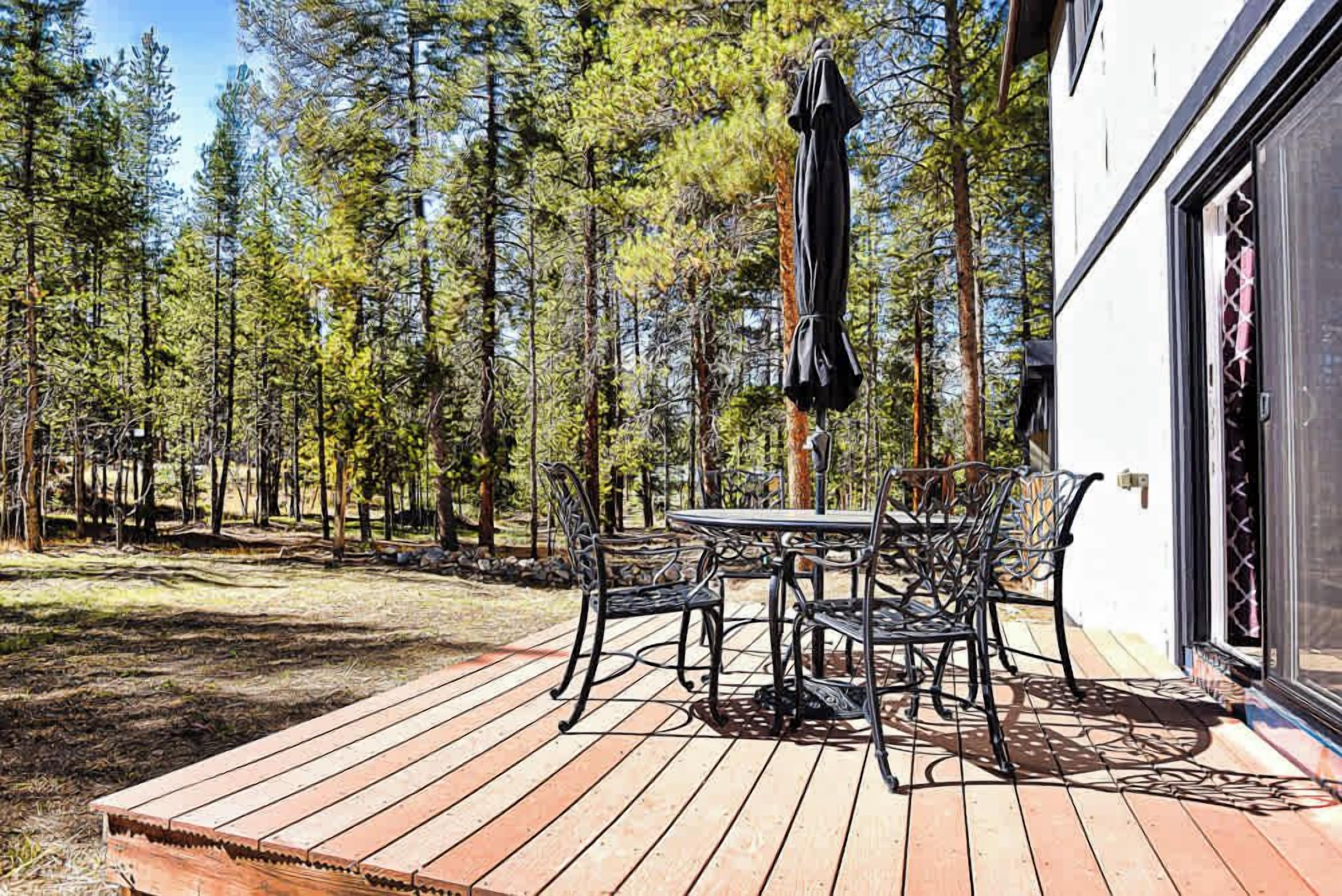 A deck with a table and chairs, surrounded by a forest.