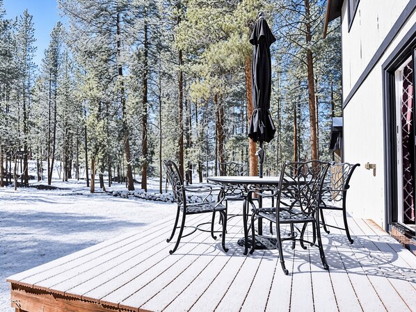 Una terraza de madera con una mesa y sillas, rodeada de árboles cubiertos de nieve.