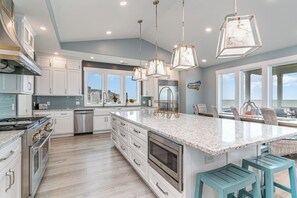 A modern kitchen with white cabinetry, a large island, stainless steel appliances, and pendant lighting. - Anchor of the Soul: Oceanfront Luxury w/private pool & Amenities (Murrells Inlet)