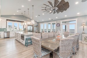 A spacious kitchen with a large island, modern appliances, and a dining area with wicker chairs and a glass table. - Anchor of the Soul: Oceanfront Luxury w/private pool & Amenities (Murrells Inlet)
