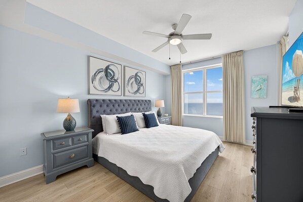 A bedroom with a large bed, a ceiling fan, and artwork on the walls.