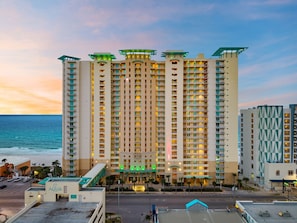 A high-rise hotel with multiple balconies, a prominent entrance, and a view of the ocean.