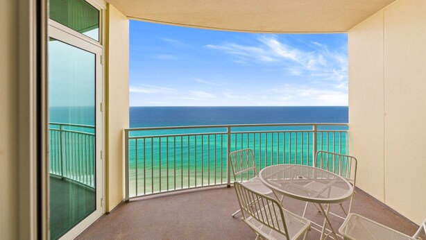 A balcony with a table and chairs, overlooking a clear blue ocean.