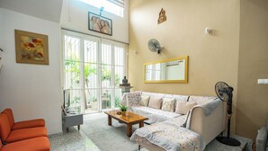 A living room with a sofa, a coffee table, and a chair. There is a window with a view of greenery outside.