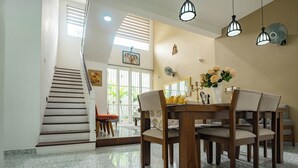 A dining area with a wooden table and chairs, a vase with flowers, and a staircase leading to another room.