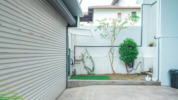 Une cour étroite et pavée, avec une porte de garage fermée, un petit arbre et un mur blanc.