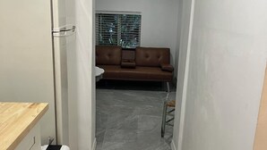 A kitchen with a refrigerator, a wooden countertop, and a dishwasher. There is a living area with a brown sofa and a window with blinds. - Charming 1-bedroom apartment in delightful Biscayne Park (North Miami)