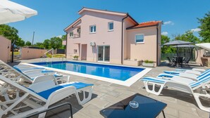 Una casa de dues plantes amb piscina, gandules i moble d'exterior.