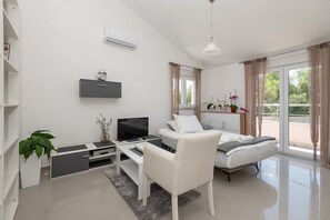 A modern, well-lit room with a bed, a TV, a desk, and a chair. There is a window with curtains, a plant, and a shelf with flowers. - Villa Bianca with private pool (Gornji Vinjani)