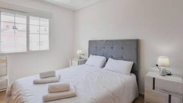 A minimalist bedroom with a large bed, two bedside tables, and a window providing natural light.