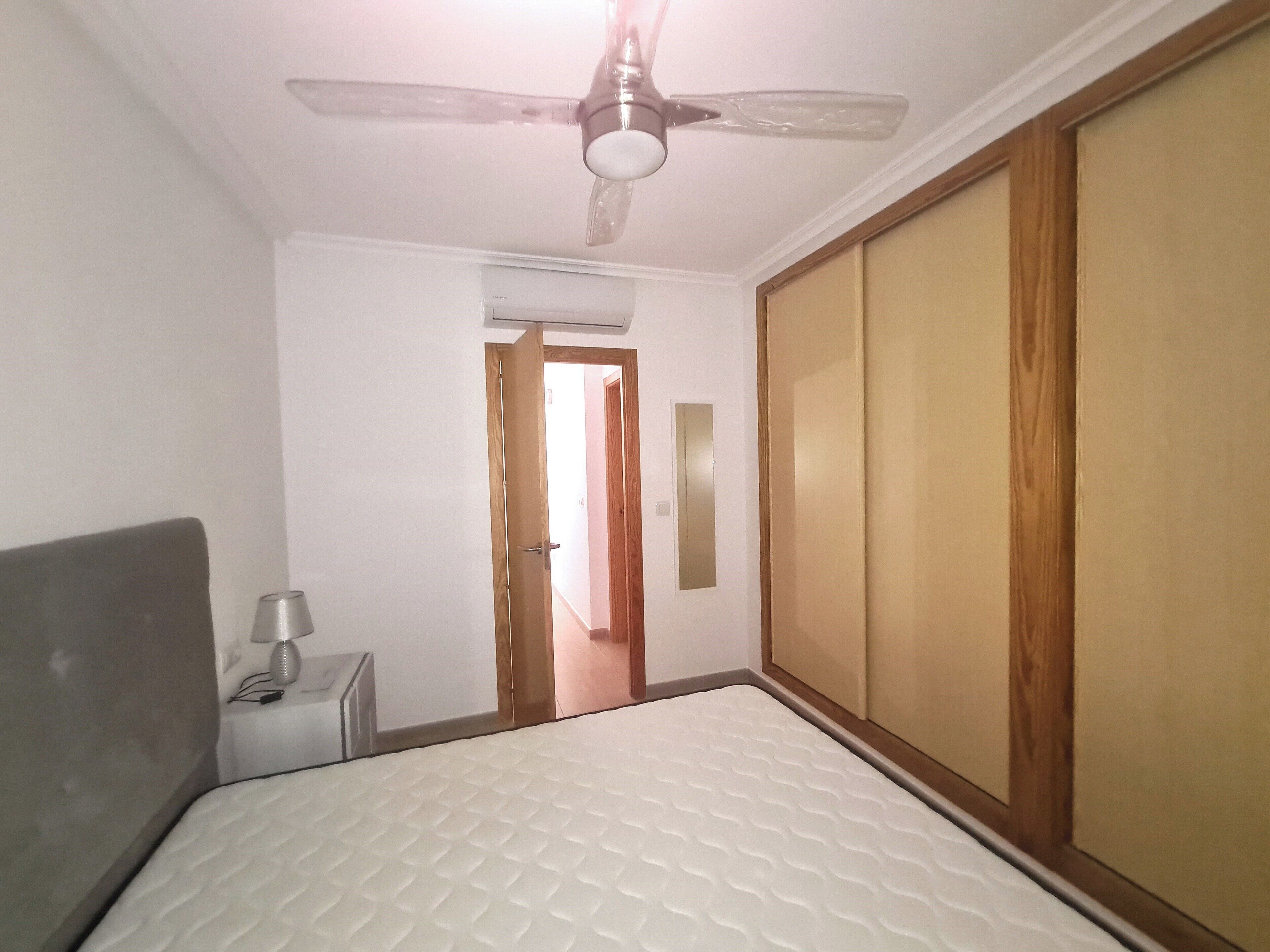 A bedroom with a bed, a bedside table, a ceiling fan, and a wardrobe.