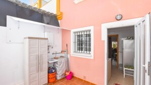 Una cucina compatta con un armadietto bianco, una finestra con sbarre e un'uscita verso una sala da pranzo.