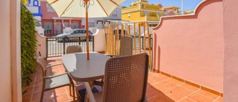 Een terras met een tafel en twee stoelen, een witte parasol, en een uitzicht op de straat en gebouwen op de achtergrond.