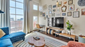 A modern living room with a blue sofa, a wooden coffee table, and a TV on a wooden stand. - Modern Condo With Mountain Views, Walk To Downtown 2 Bedroom Condo (Salt Lake City)