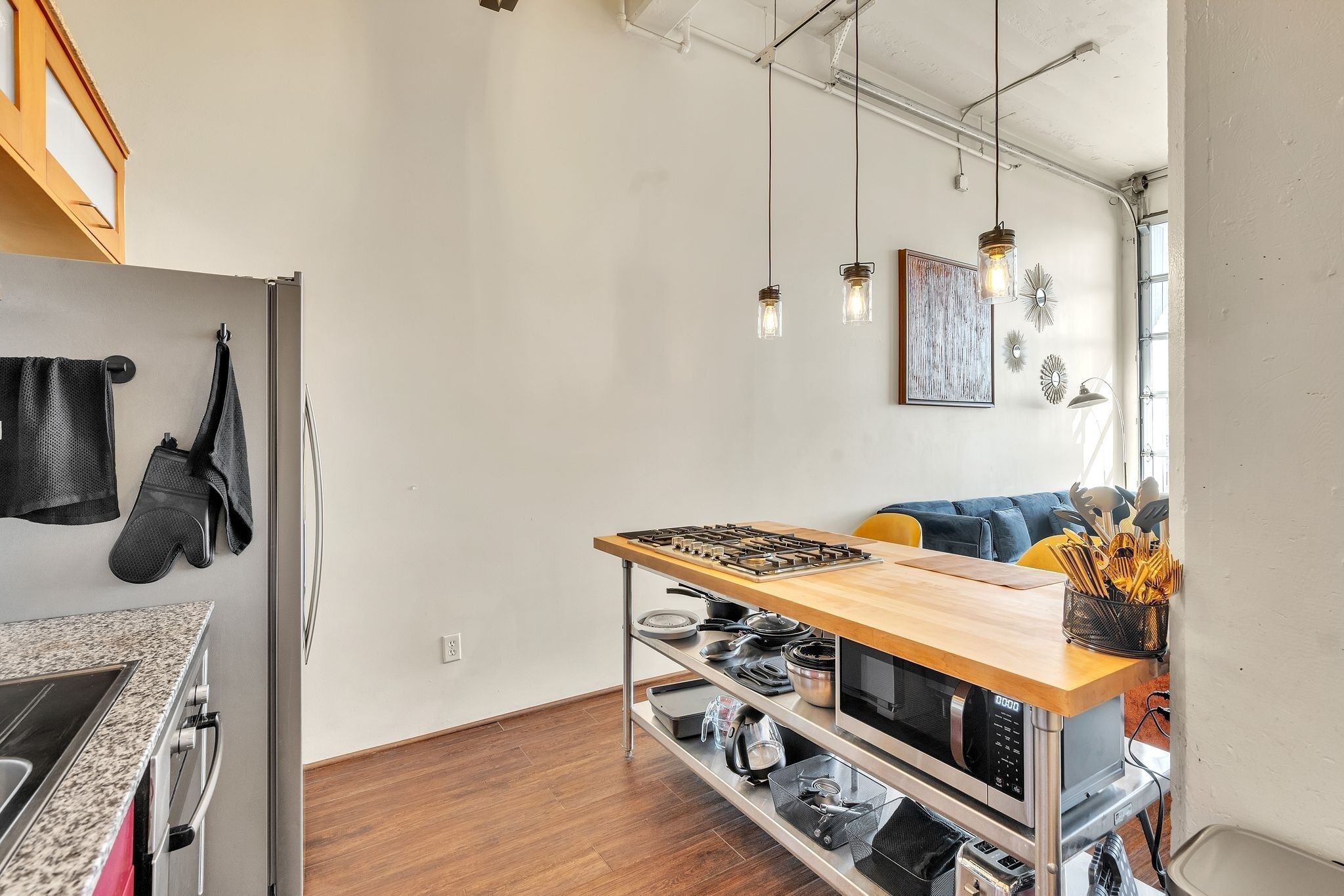 A compact kitchen with a wooden countertop, stainless steel appliances, and hanging lights.