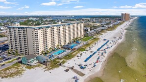 Un hôtel situé sur la côte, avec plusieurs étages, une piscine et une plage équipée de parasols.