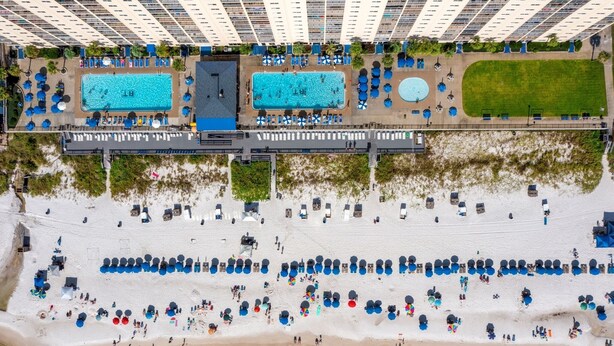 Vue aérienne d’un hôtel doté de plusieurs piscines, d’une plage avec des transats et d’un grand espace herbeux.