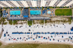 Vue aérienne d’un hôtel doté de plusieurs piscines, d’une plage avec des transats et d’un grand espace herbeux.