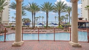 A pool area with palm trees, a pool, and a building in the background. - Waterfront condo w/ pool & beach access (Panama City Beach)