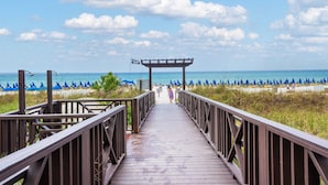A wooden boardwalk leading to a beach with blue umbrellas and a clear sky. - Waterfront condo w/ pool & beach access (Panama City Beach)