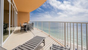 A balcony with a table and chairs, a view of the ocean, and a white railing. - Phoenix Gulf Towers 2007 3 Bedroom Condo (Orange Beach)