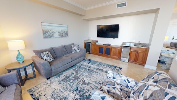 A living room with a sofa, a coffee table, a rug, a TV, and a kitchen area with cabinets and appliances.