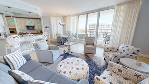 A modern living room with a grey sofa, patterned ottoman, and white armchairs. A dining area with a table and chairs is visible in the background. - St. Maarten Penthouse 1 3 Bedroom Condo (Destin)