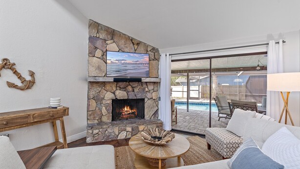 A living room with a stone fireplace, a television mounted above it, and a view of a pool through large glass doors. - Mauna Loa Hideaway 3 Bedroom Home (Sarasota)