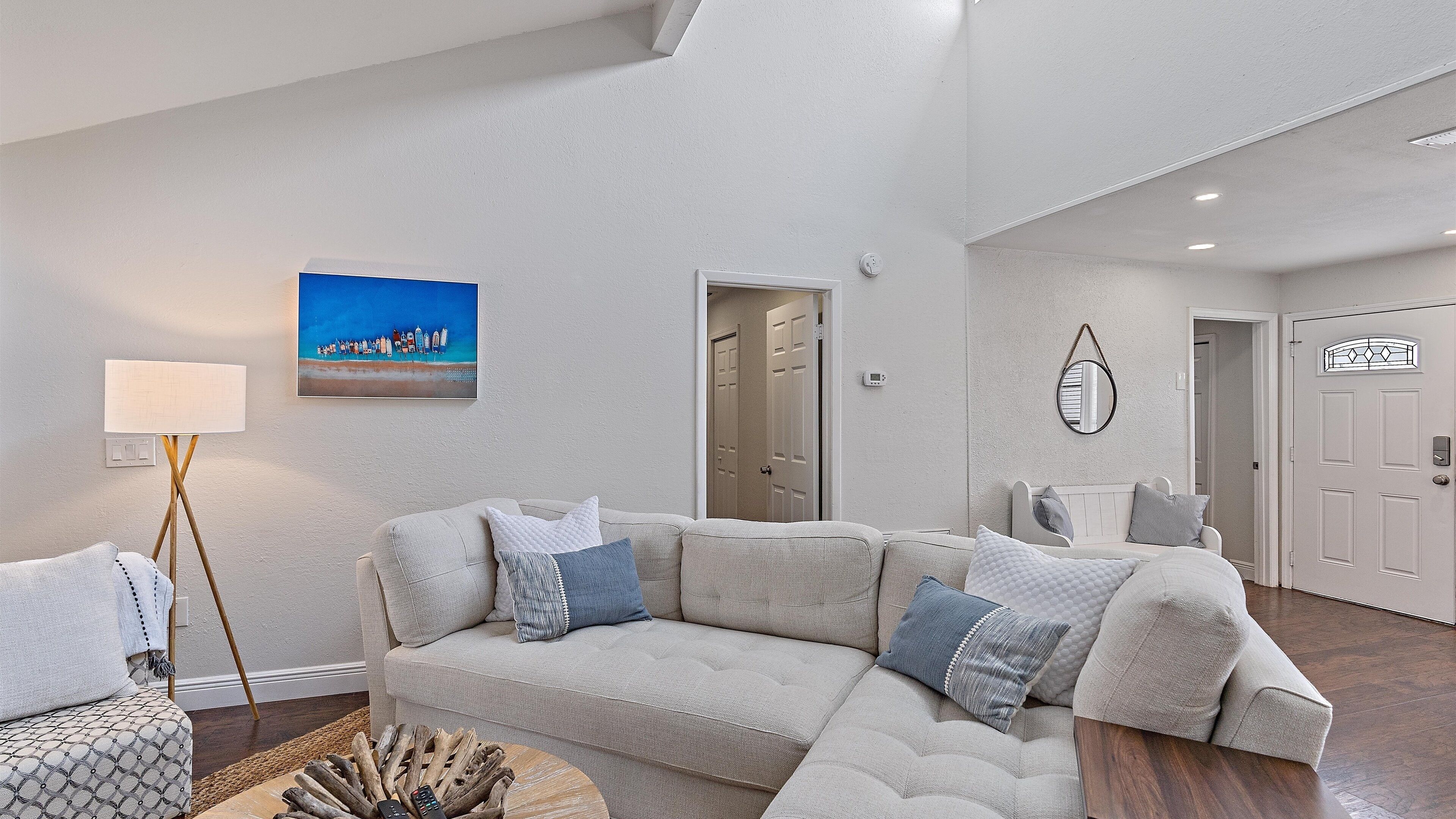 A spacious living room with a large sectional sofa, a floor lamp, and a painting of a beach scene.