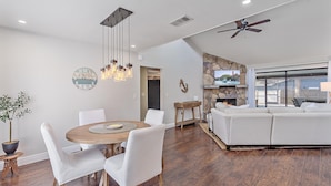 A modern living room with a fireplace, a dining area with a round table, and a large window overlooking a deck. - Mauna Loa Hideaway 3 Bedroom Home (Sarasota)