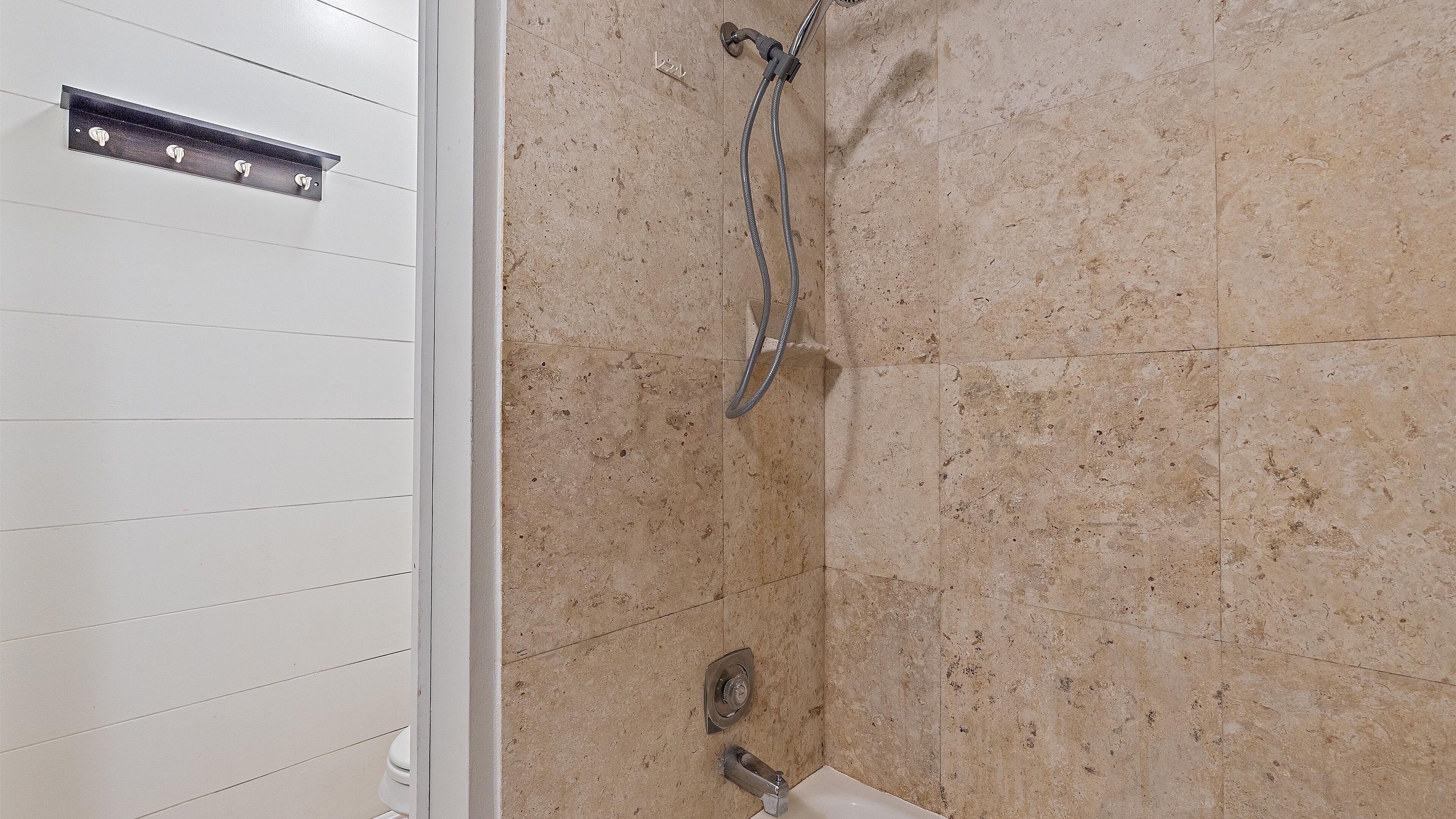 Un baño con ducha, paredes de azulejos y una puerta blanca.