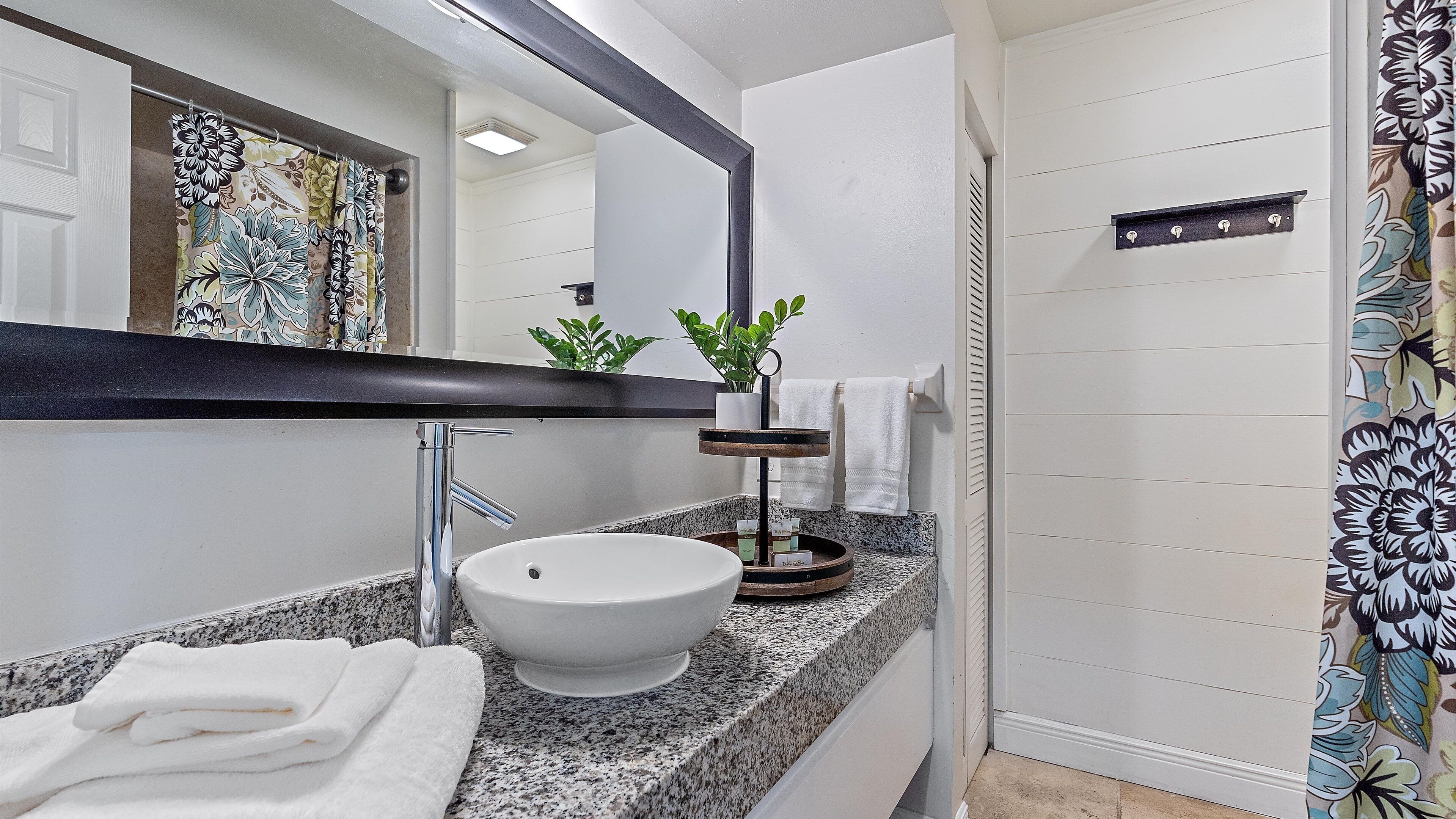 A bathroom with a white sink, a mirror, a towel rack, and a shower curtain with a floral pattern.