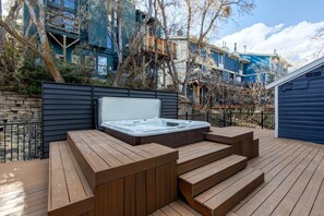 A wooden deck with a hot tub, stone wall, and a view of a blue building with balconies. - Blue Church Lodge C 2 Bedroom Condo (Park City)